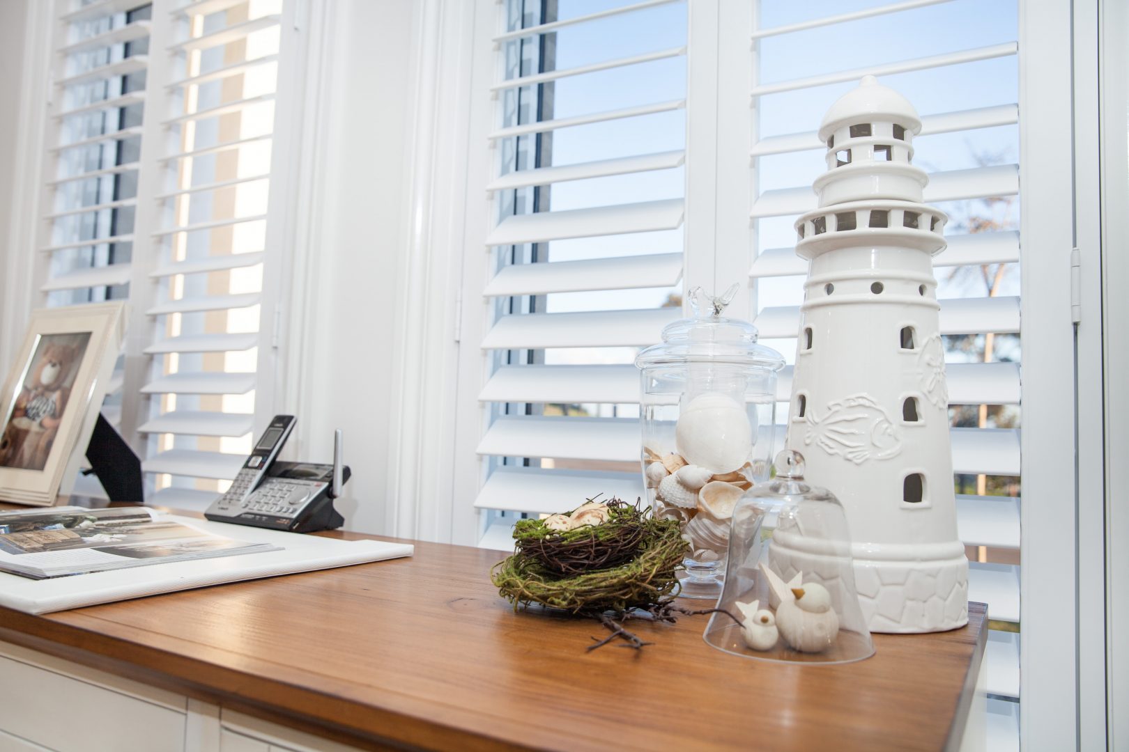 Close up of white shutters open in an office space with a timber desk top and white tower figurine 