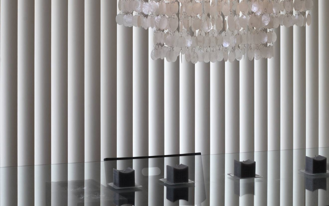 Close up of grey vertical blinds semi closed with a white shell chandelier 