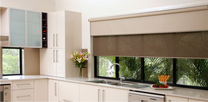 Modern kitchen featuring neutral-toned roller blinds, white cabinetry, and stainless steel appliances, with a large window offering views of outdoor greenery