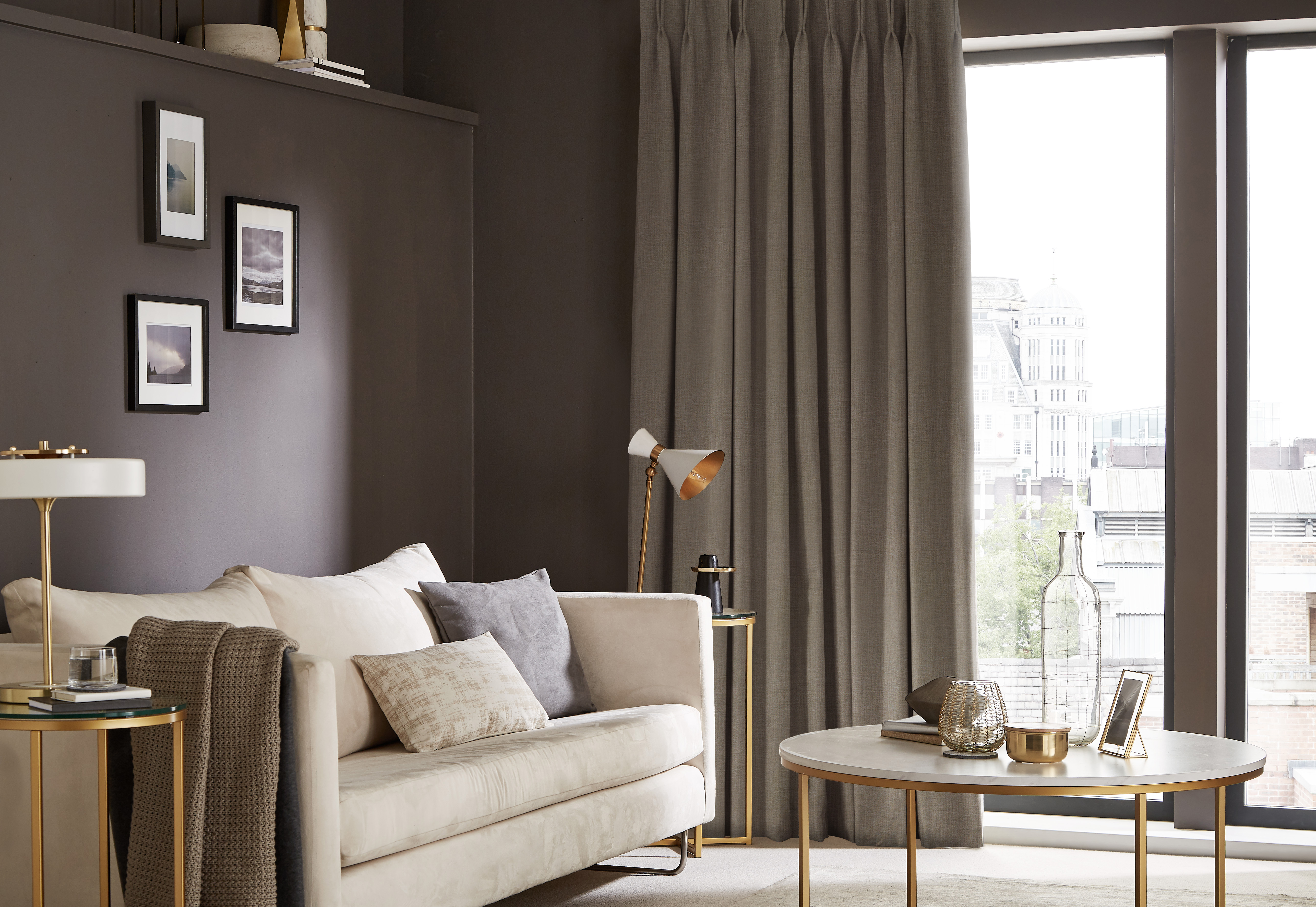 Chic living room with dark grey double pleat curtains, a light beige sofa with accent pillows, gold side tables, and a round coffee table