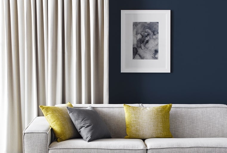 A living room with a grey couch and a navy wall complimented by a cream blockout curtain