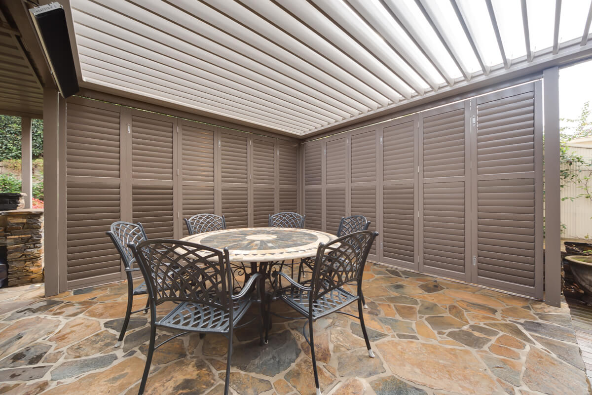 Aluminium shutters surrounding an outdoor dining area with round table and chairs