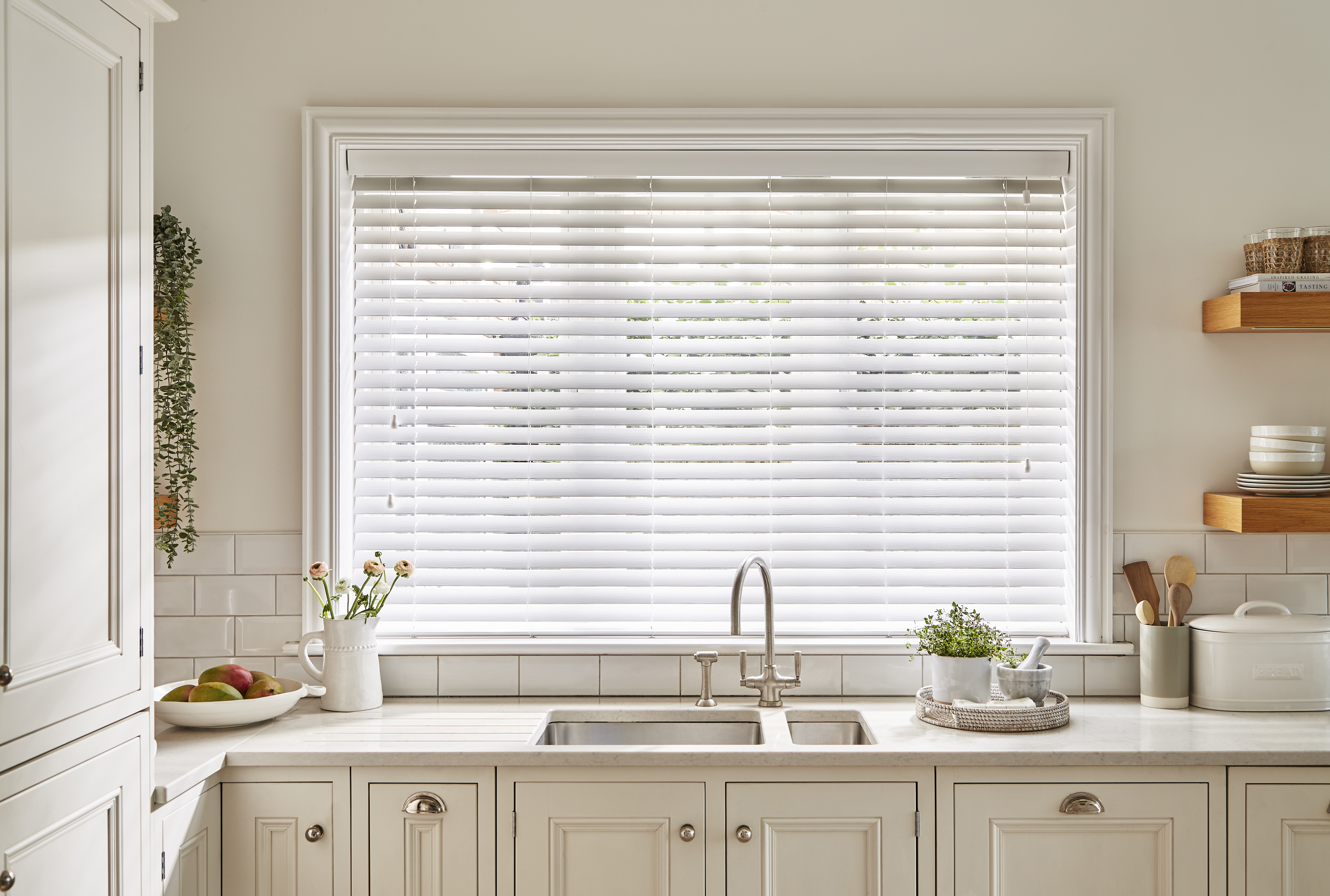 Bright kitchen featuring faux wood Venetian blinds in ultra-white, providing a clean, classic look above a farmhouse sink and neutral cabinetry