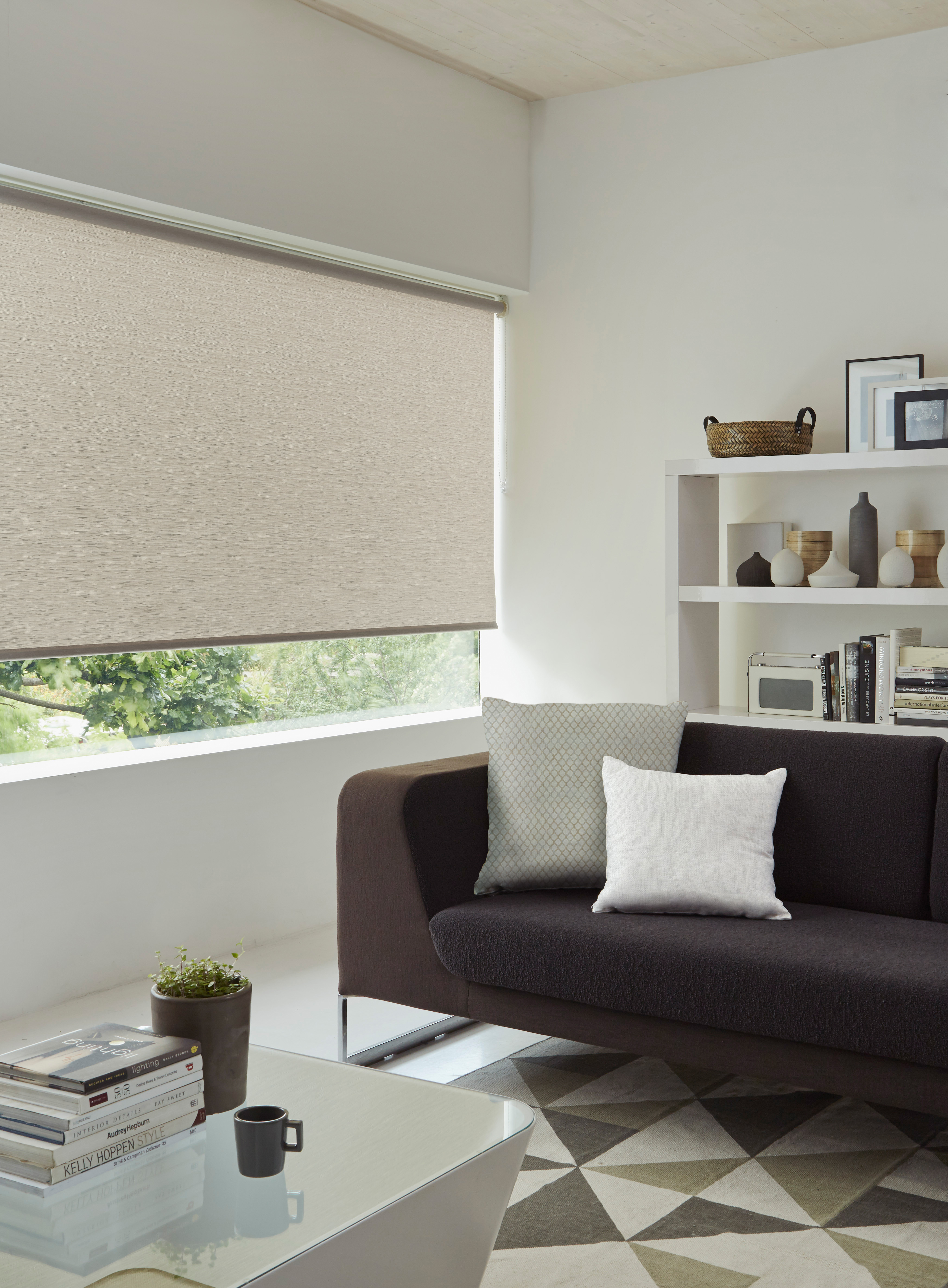 Modern living room with a beige textured roller blind, a dark sofa with neutral pillows, and a geometric rug, creating a stylish and comfortable space
