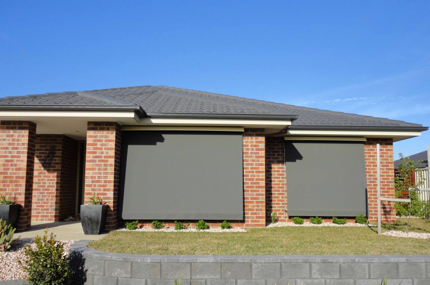 Brick house with grey outdoor awnings covering the windows, providing shade and privacy while maintaining a sleek, modern look