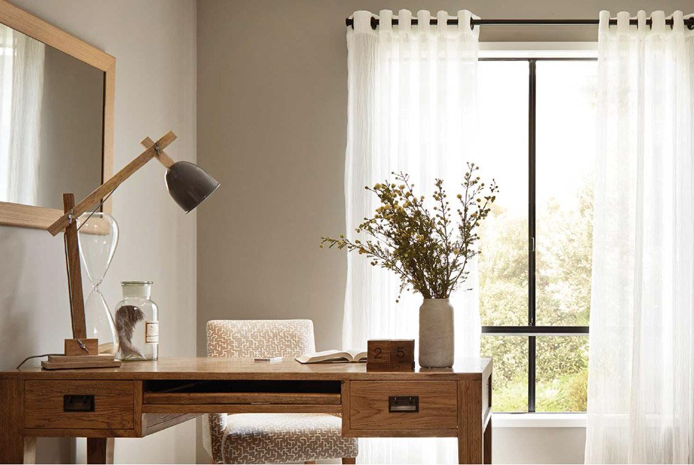 Neutral study with timber desk and cream chair and grey vase of flowers complimented by white sheer eyelet curtains