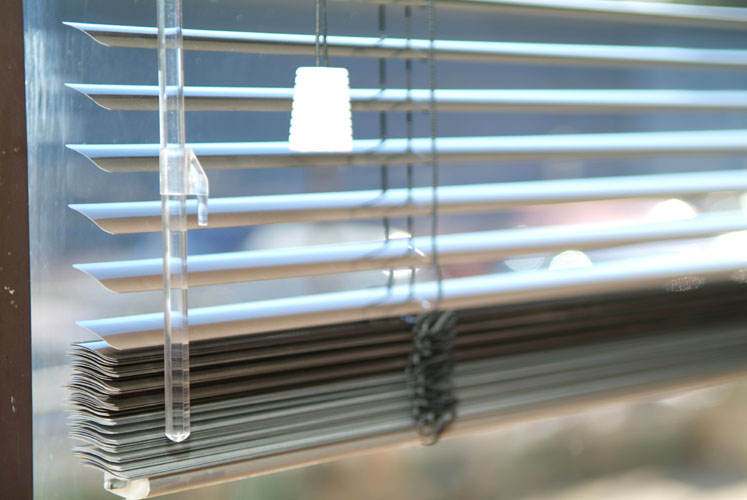 Close up of fully opened aluminum Venetian blinds with a plastic hanging cord