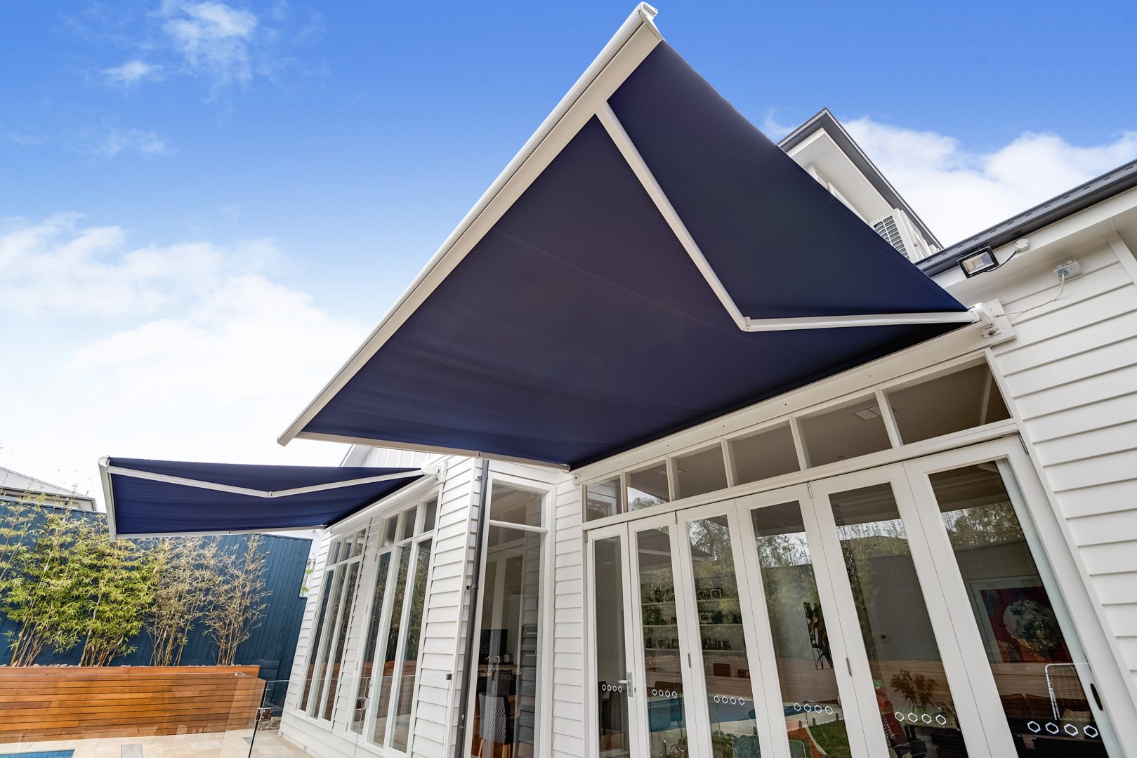 Open navy and white folding arm awning over a white framed glass door and connected to a white paneled house