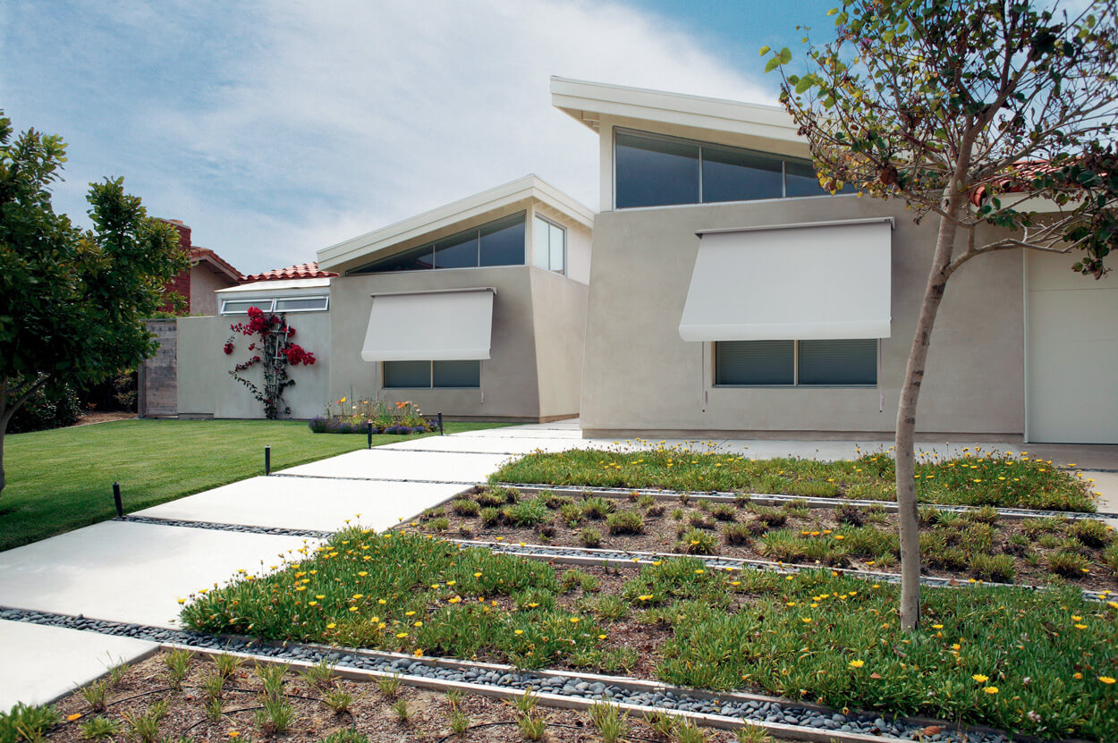 Cream one storey house with a larger, green lawn and white awnings on the front windows