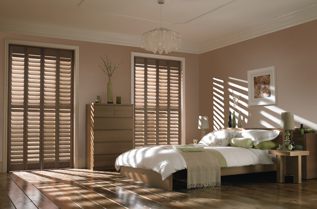Vintage oak dark brown full height shutters fitted to two windows in a wood & beige decorated bedroom
