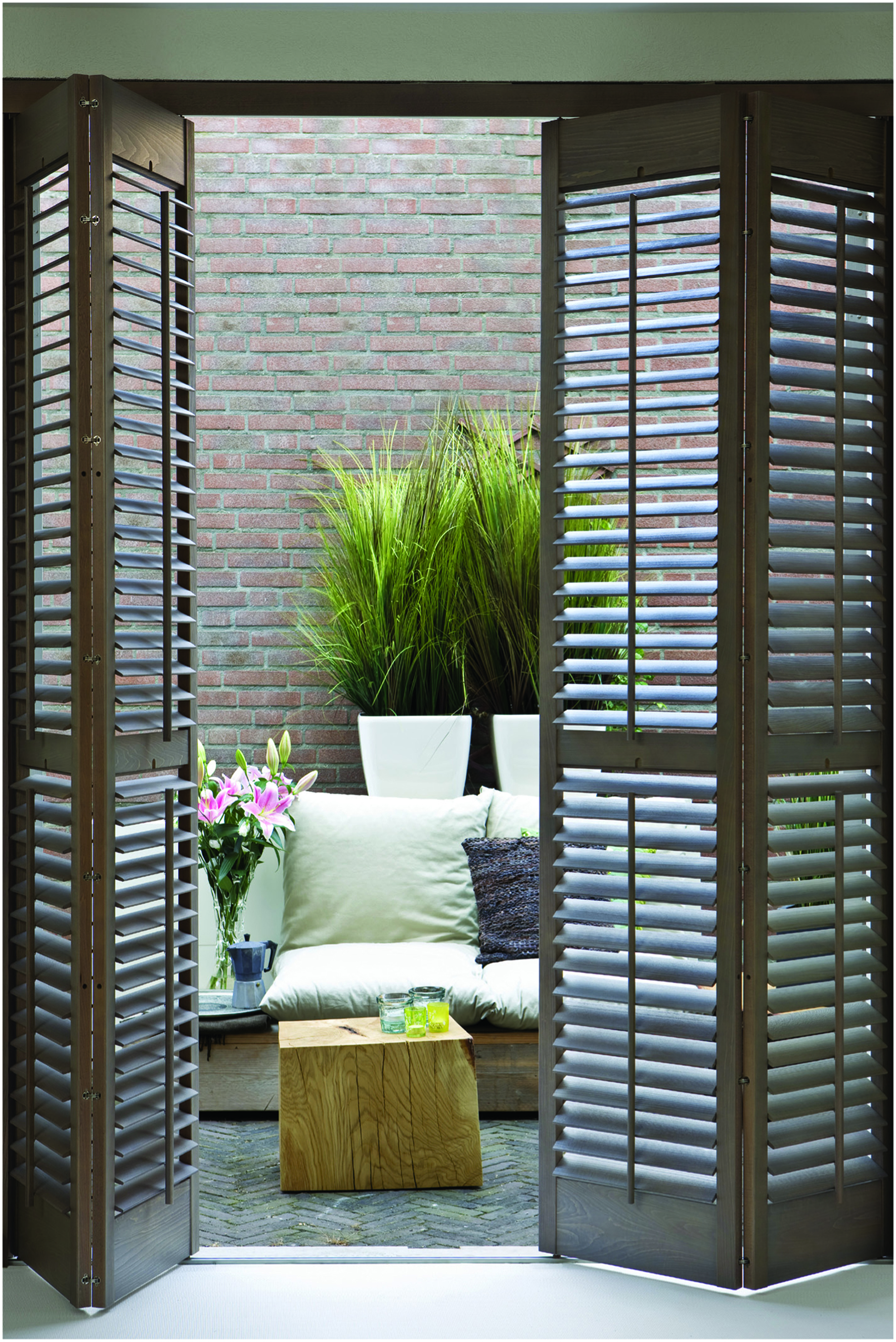 Timber bi fold shutters opened up to an outdoor living space with a brick wall and white couch