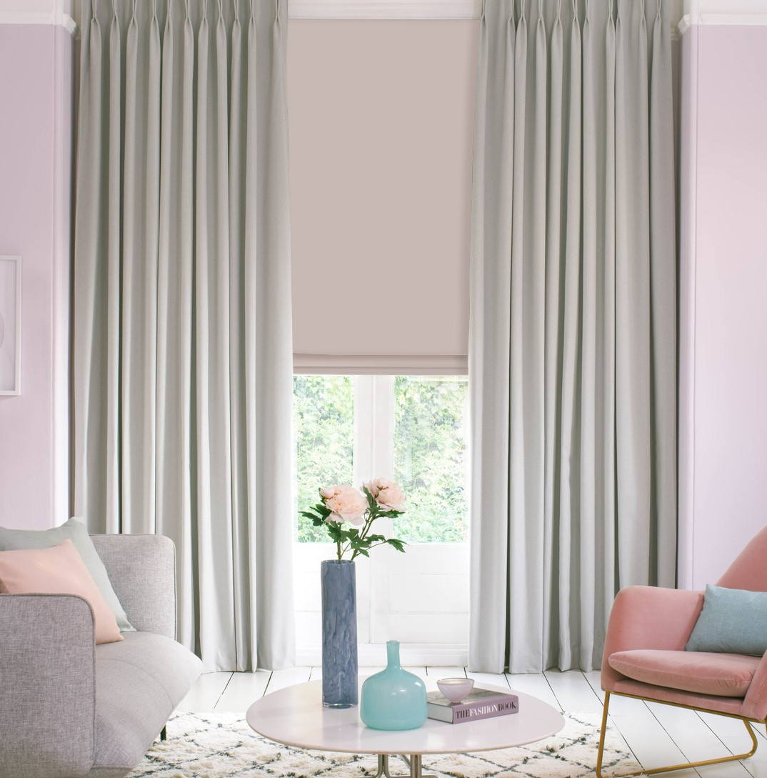 Bright living room with grey couch, pink chair, light pink walls and light grey pinch pleat curtains