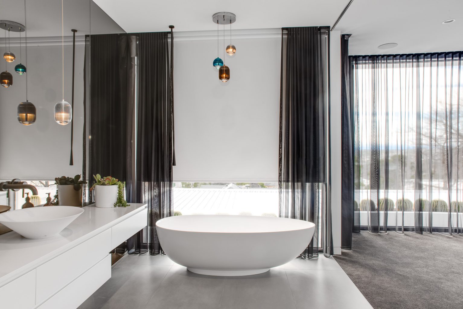 Luxurious bathroom with white freestanding bathtub, sheer black curtains, and modern roller blinds