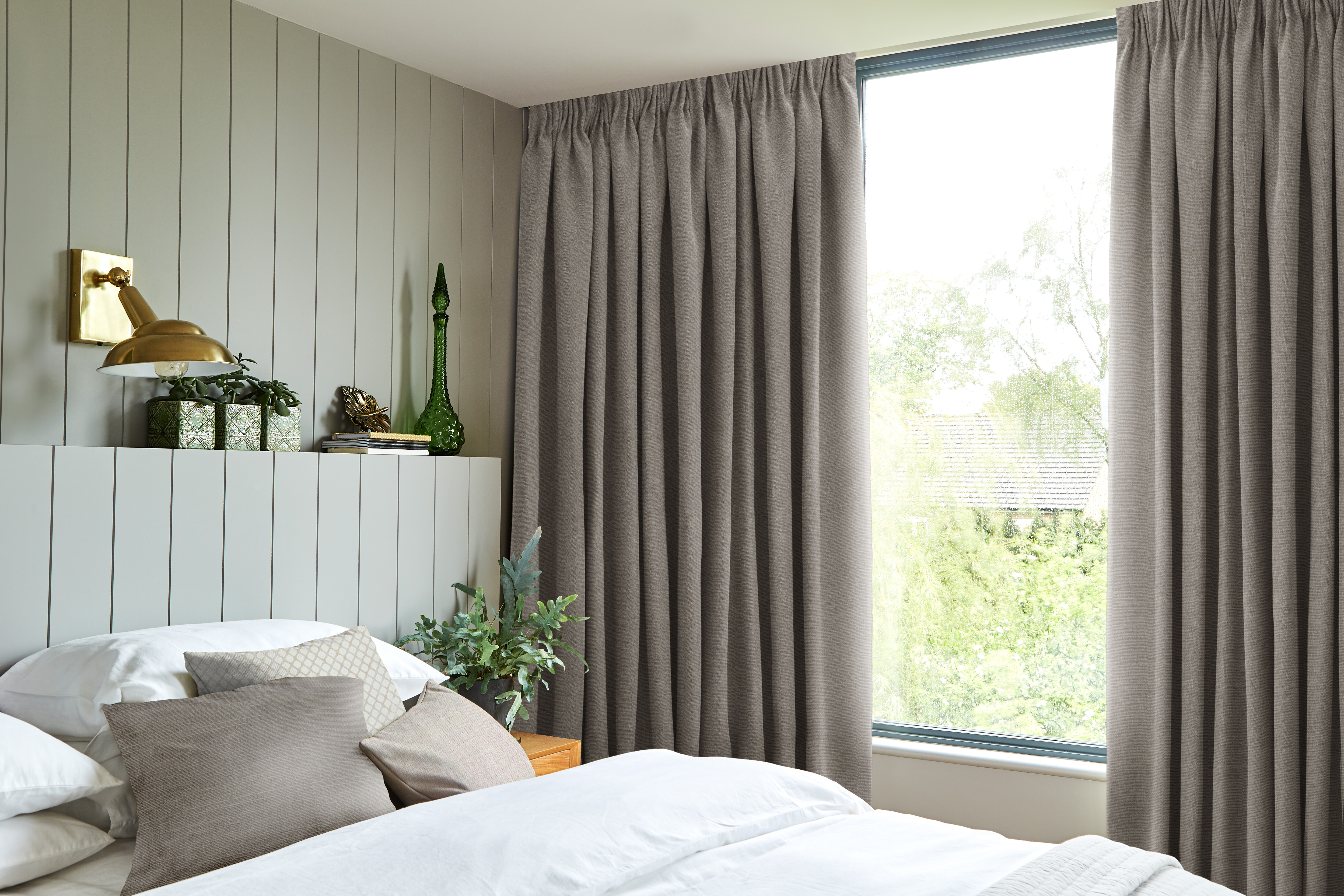 Bedroom with soft grey pinch pleat curtains, a neatly made bed with neutral-toned pillows, and minimalist decor, offering a serene and natural atmosphere