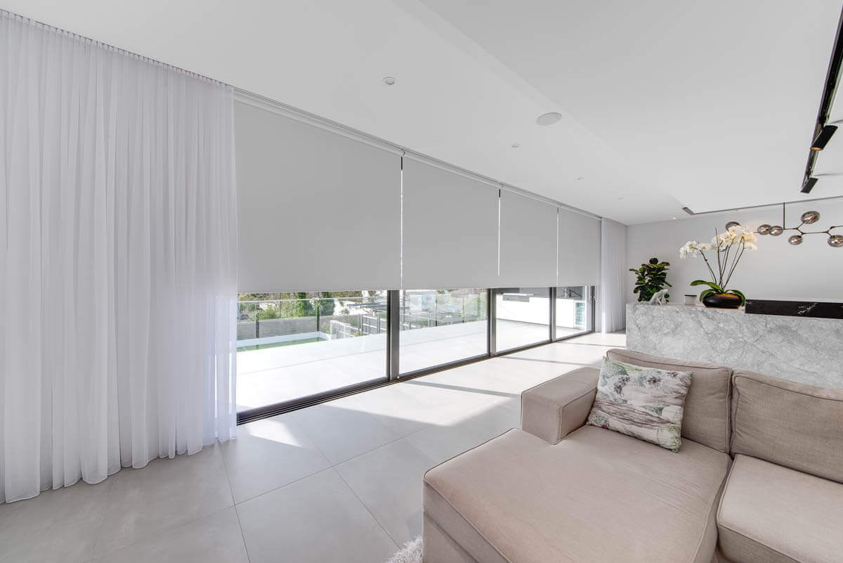 A living room with a blush couch and white sheer curtains with a white roller blind