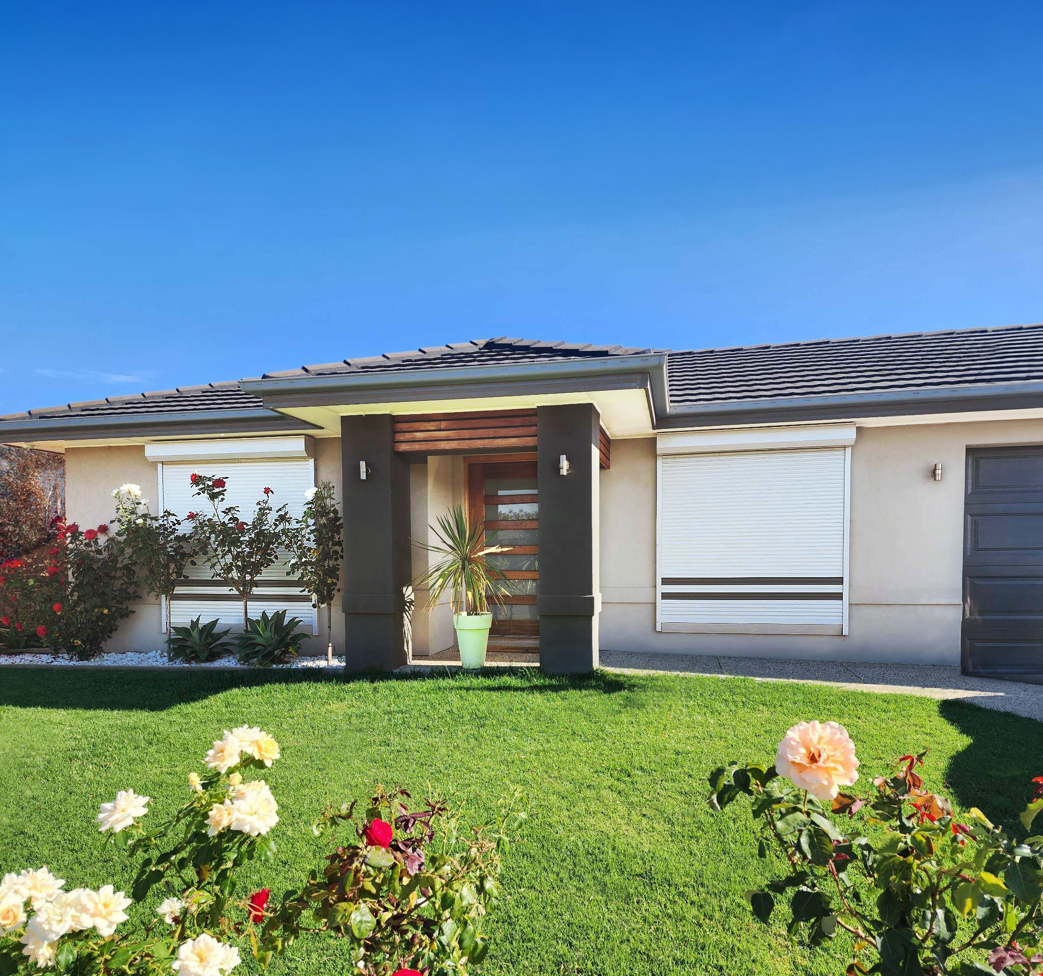 Cream roller shutters on the front windows of a cream and charcoal coloured one storey home
