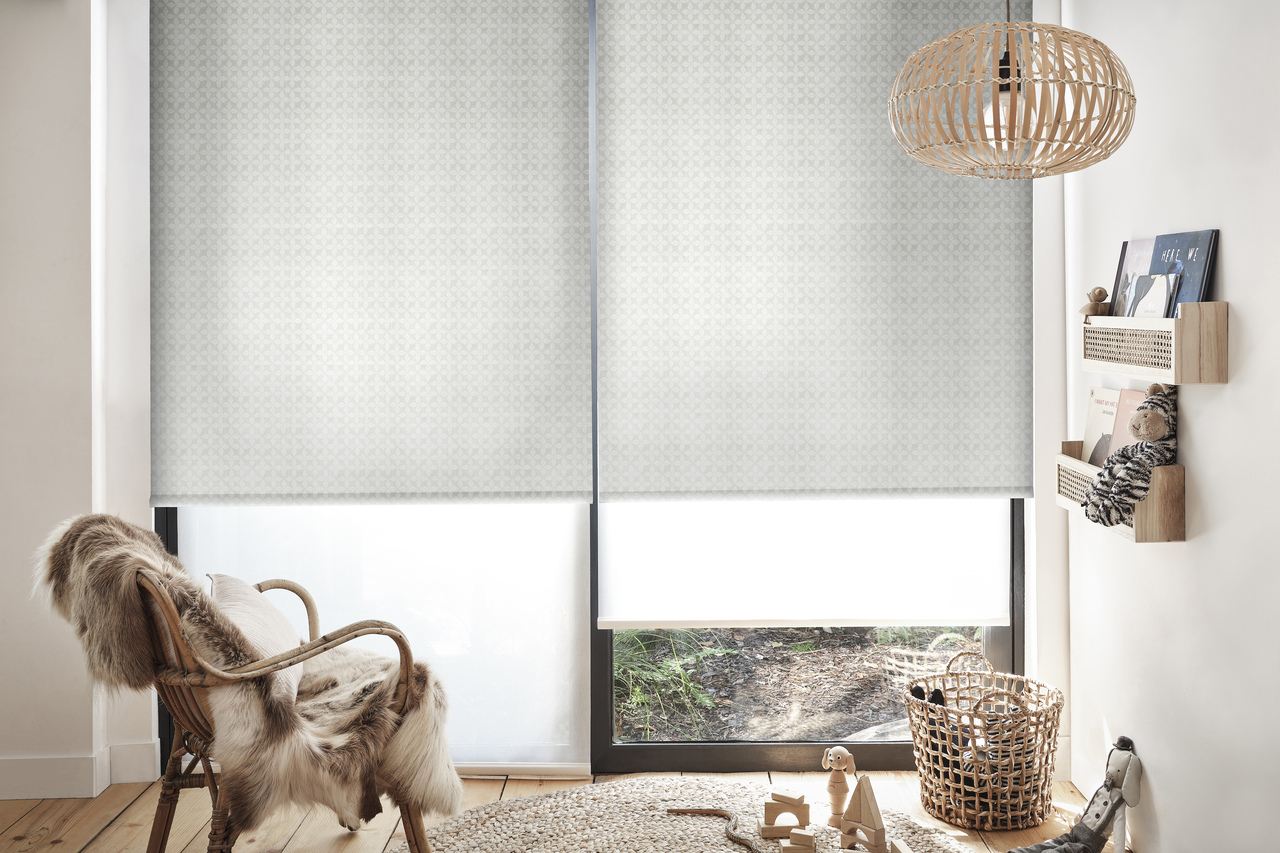 A room with a chair and a window featuring grey translucent roller blinds
