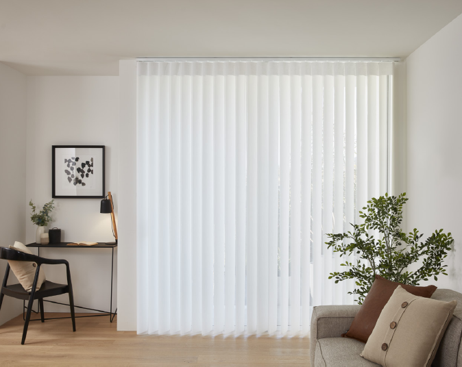 Cream veri shade blinds closed in a room with a dark timber desk and chair and light grey couch