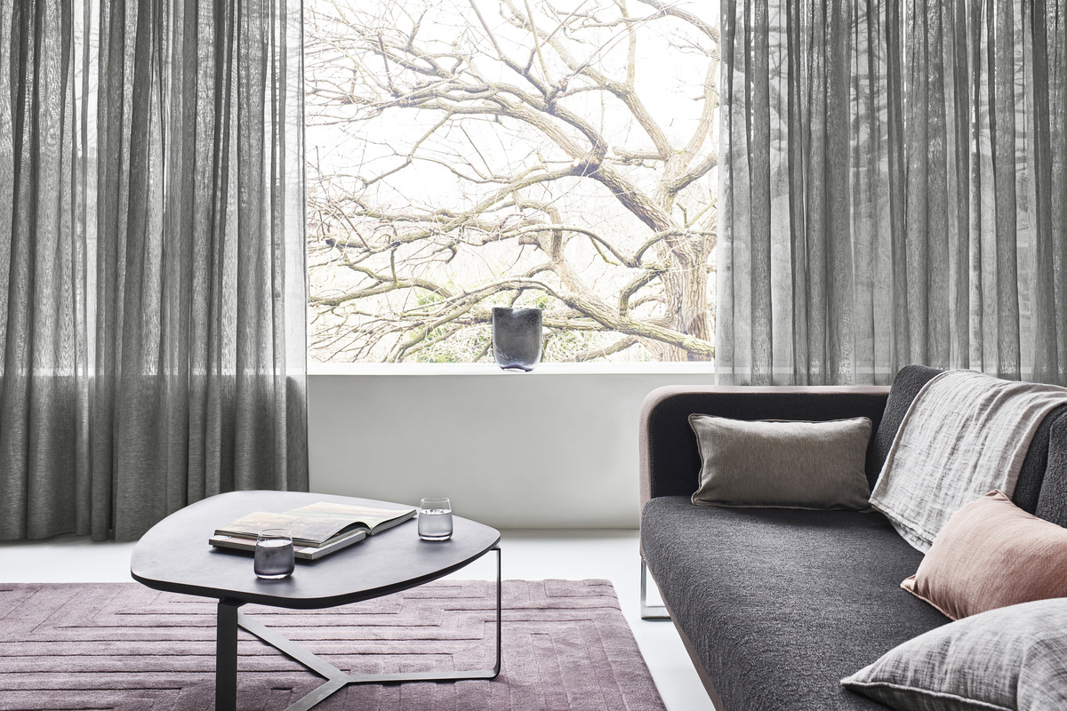 Dark grey sheer curtains in a neutral living room with a grey couch, coffee table and blush rug