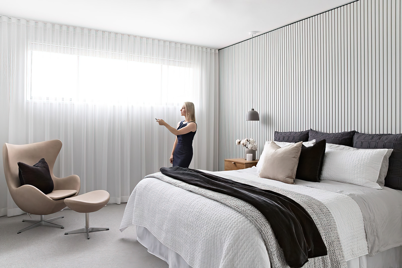 Woman operating motorised sheer curtains in a modern bedroom