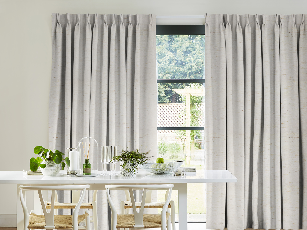 Bright dining space with pleated light grey curtains, a white dining table adorned with plants and glassware
