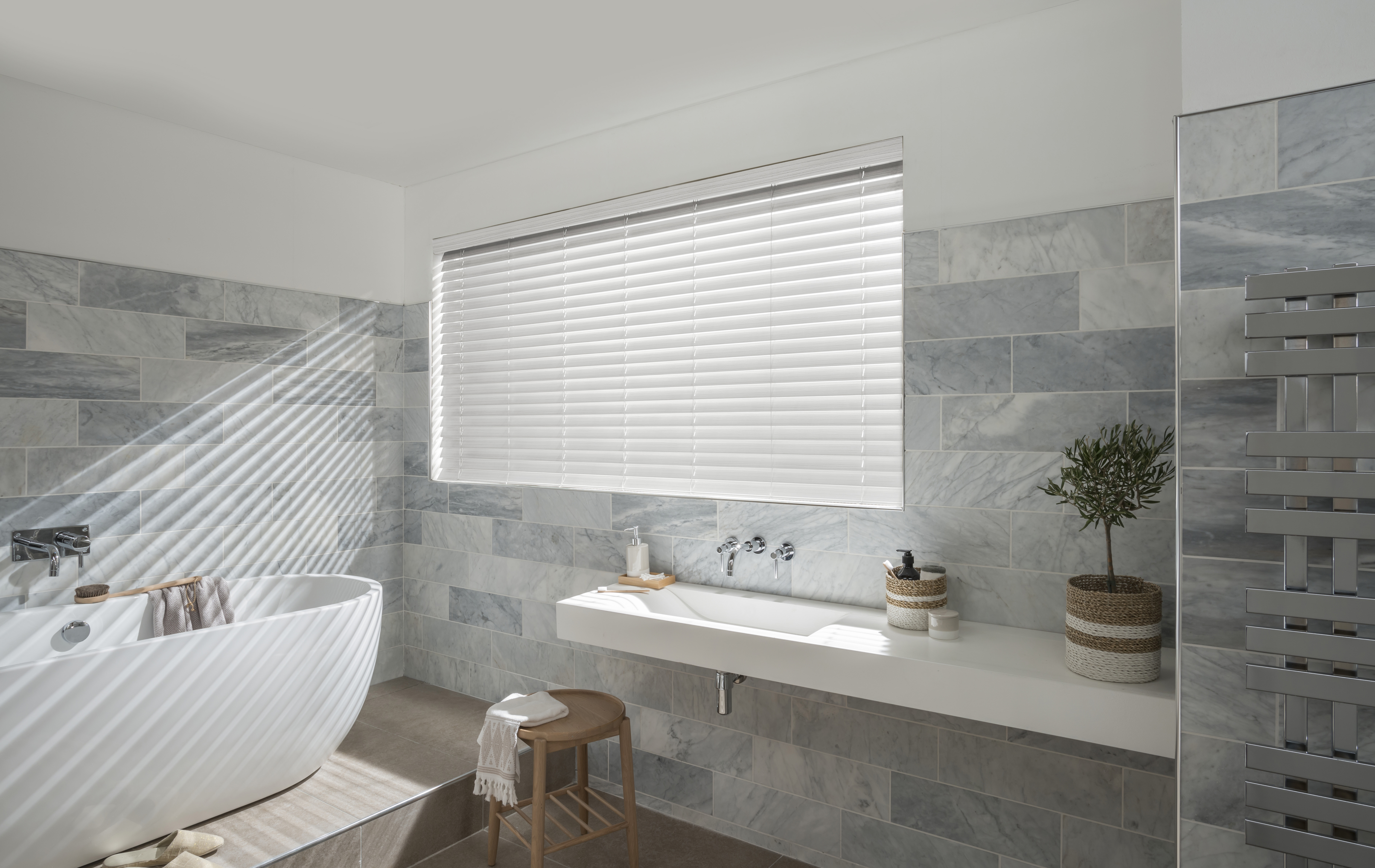 Grey marble tiled bathroom with white egg bath and basin complimented by white PVC venetian blinds
