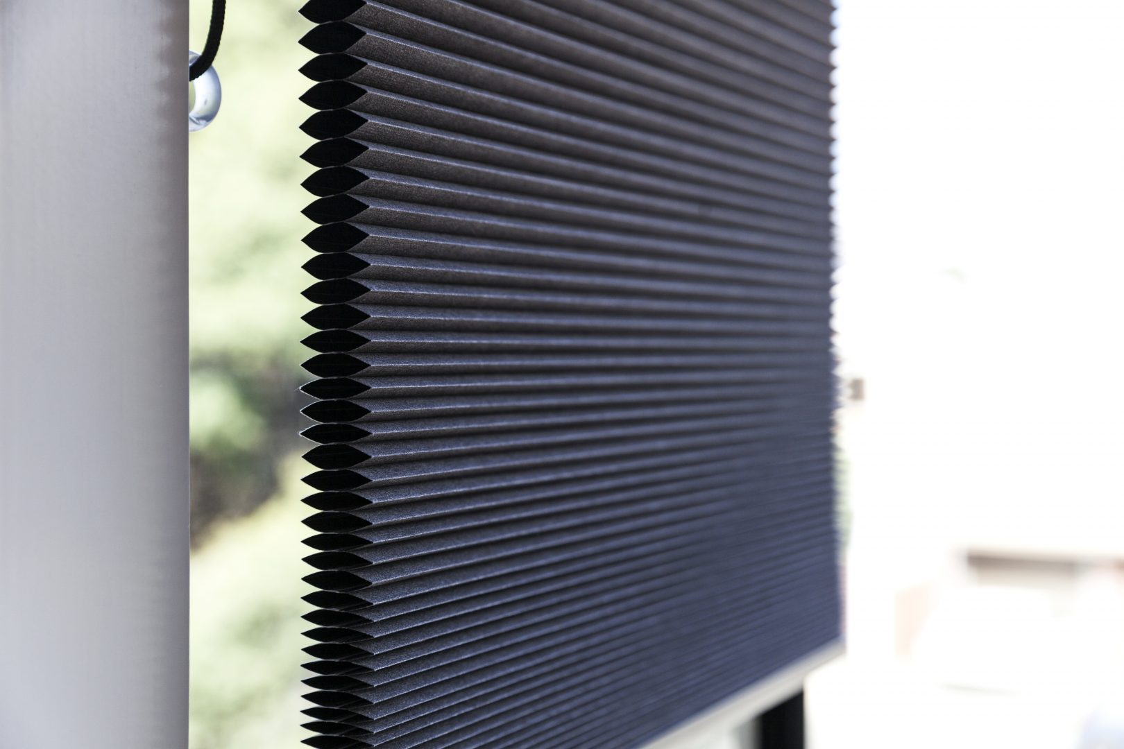 Close-up-of-black-cellular-blinds-with-honeycomb-structure,-leaving-a-side-gap-against-the-wall