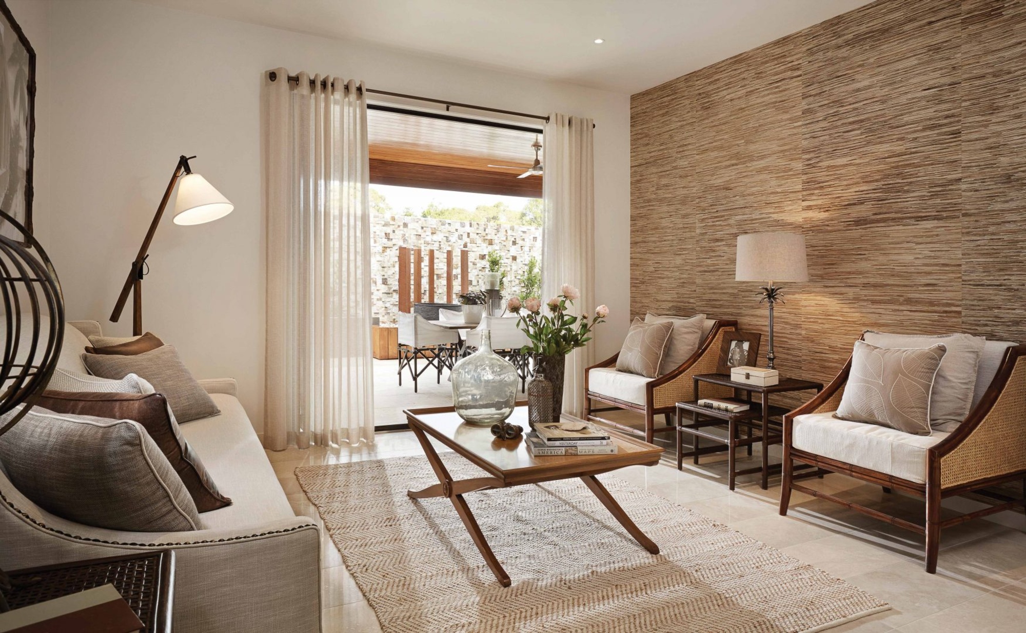 Neutral living room with grey couch and two beige and brown chairs complimented by cream sheer eyelet curtains